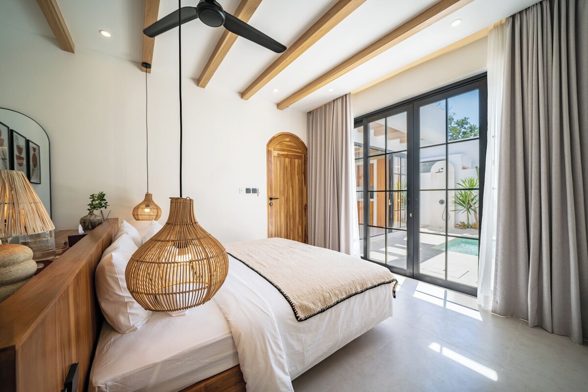 A modern bedroom with a large bed, a ceiling fan, and a view of a swimming pool through a glass door.