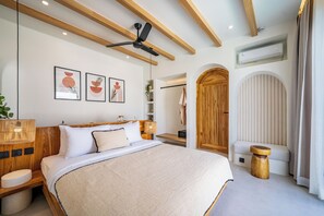 A modern bedroom with a large bed, wooden beams, ceiling fan, and framed artwork on the wall. - Villa Raya & Villa Viora Uluwatu (Pecatu)