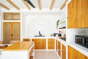 A modern kitchen with wooden cabinets, a central island, and a built-in microwave. - Villa Raya & Villa Viora Uluwatu (Pecatu)