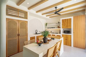 A modern kitchen with wooden cabinetry, a central island, and a ceiling fan. - Villa Raya & Villa Viora Uluwatu (Pecatu)
