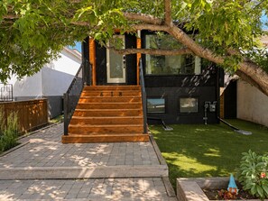 Een modern huis met een houten trap naar een zwarte deur, een verzorgd gazon en een kleine tuinbeeldje.