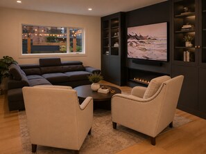 A modern living room with a sectional sofa, two armchairs, a coffee table, a fireplace, and a large TV mounted on the wall. - Cozy Stylish Home in Bridgeland (Calgary)