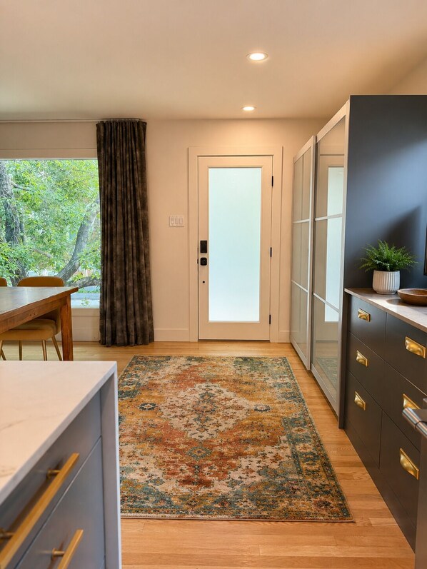 Een moderne keuken met een houten eettafel, een vloerkleed met patroon en een donkere kast met gouden handgrepen.