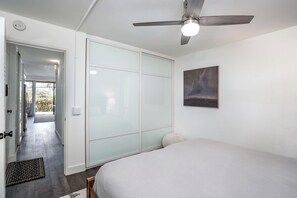 Ein Schlafzimmer mit einem Bett, einem Deckenventilator, einer Glastür zum Verschieben und einem Bild an der Wand.