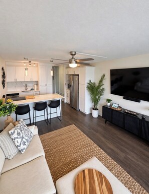 A modern living room with a sofa, a coffee table, a TV, and a kitchen area with a dining set. - “Kīhei Hideaway” @Maui Vista, 30 Sec the Beach, Ground Floor, King Bed & AC (Kihei)