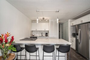 Eine moderne Küche mit einer großen Kochinsel, Barhocker, einem Kühlschrank und einer Kaffeemaschine.
