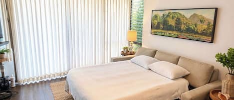 Un dormitorio con cama, sofá, ventilador de techo, ventana con cortinas y un cuadro en la pared.