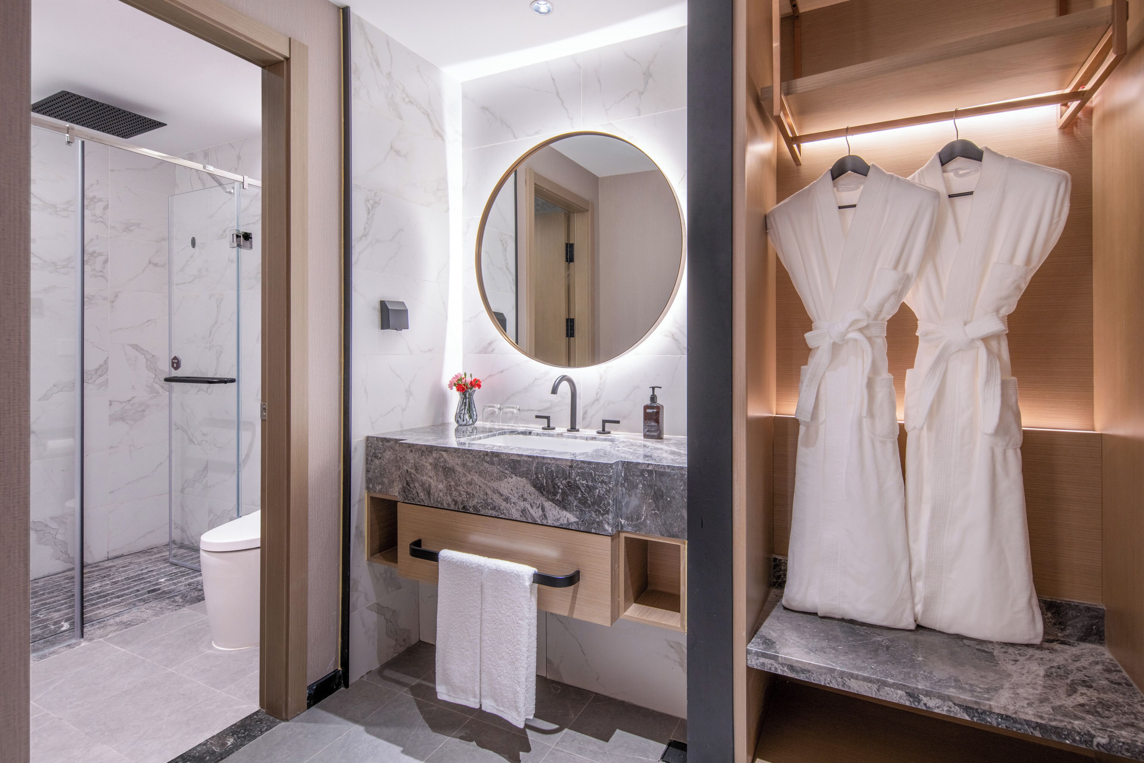 Un baño moderno con lavamanos de mármol, un espejo grande, cabina de ducha y un perchero para batas.