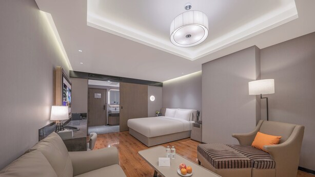 A modern hotel room with a bed, two sofas, a small table with fruit, a lamp, and a view of the bathroom. - Crystal Hotel  Beijing Guomao Heshenghui (Beijing)