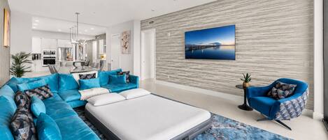 Een moderne woonkamer met een hoekbank, een enkel bed, een blauwe fauteuil en een groot schilderij aan de muur.