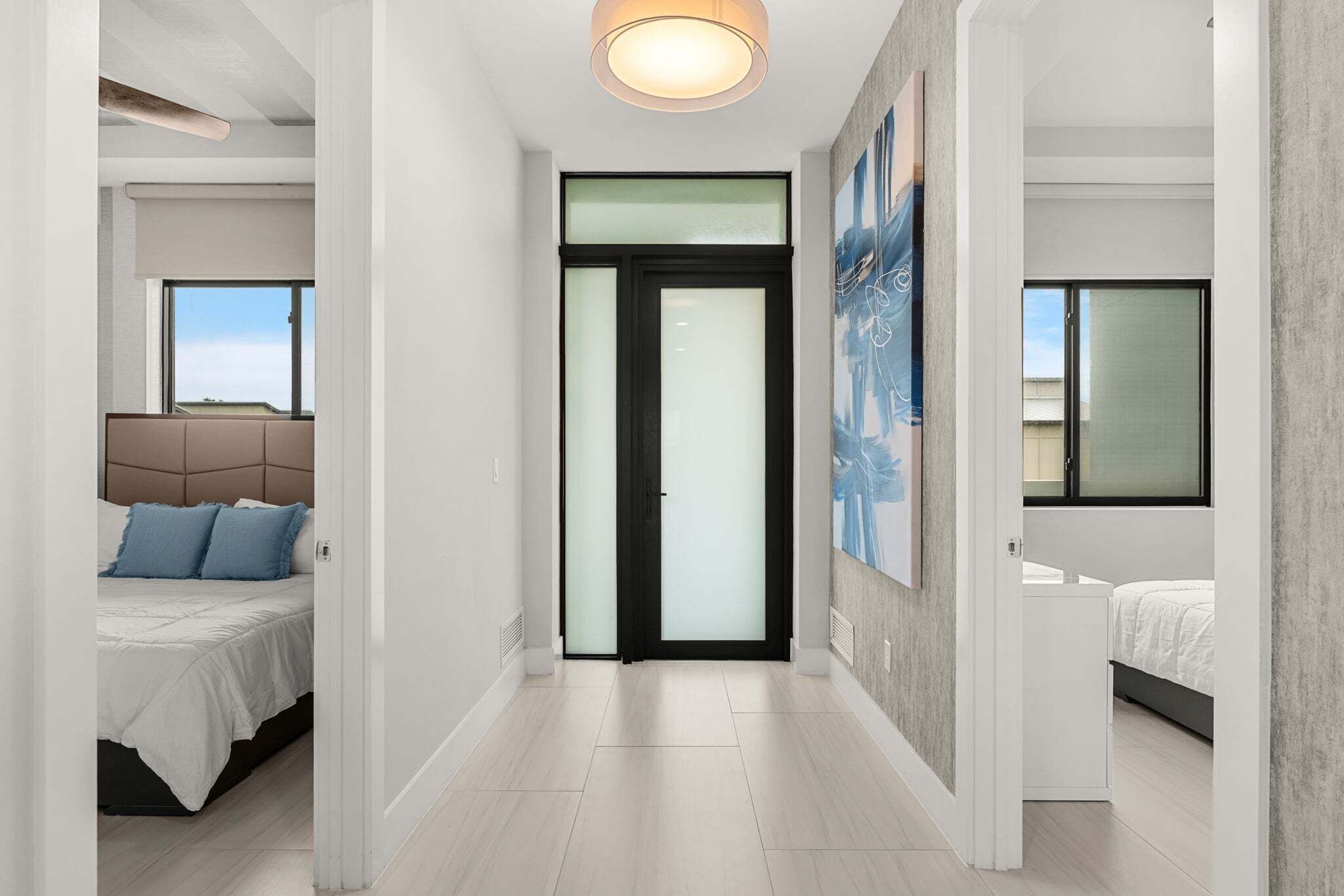 A modern hotel room with a bed, a large window, and a door leading to another room.