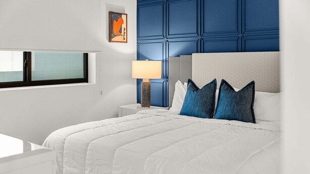 A modern hotel room with a large bed, a bedside table, a lamp, and a window. - Beautiful Melbourne Beach Retreat | Pool, Hot Tub & Private Balcony 🌴 (Melbourne Beach)