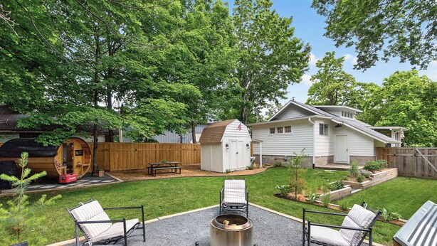 A backyard with a fire pit, two lounge chairs, a wooden shed, and a house.