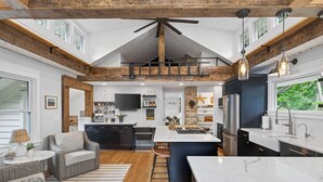 A modern kitchen with a central island, wooden beams, and a large window.