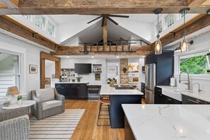 A modern kitchen with a central island, wooden beams, and a large window.