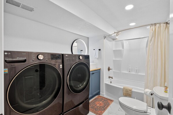 A compact laundry area with two front-loading washing machines, a small bathroom with a toilet, and a bathtub.