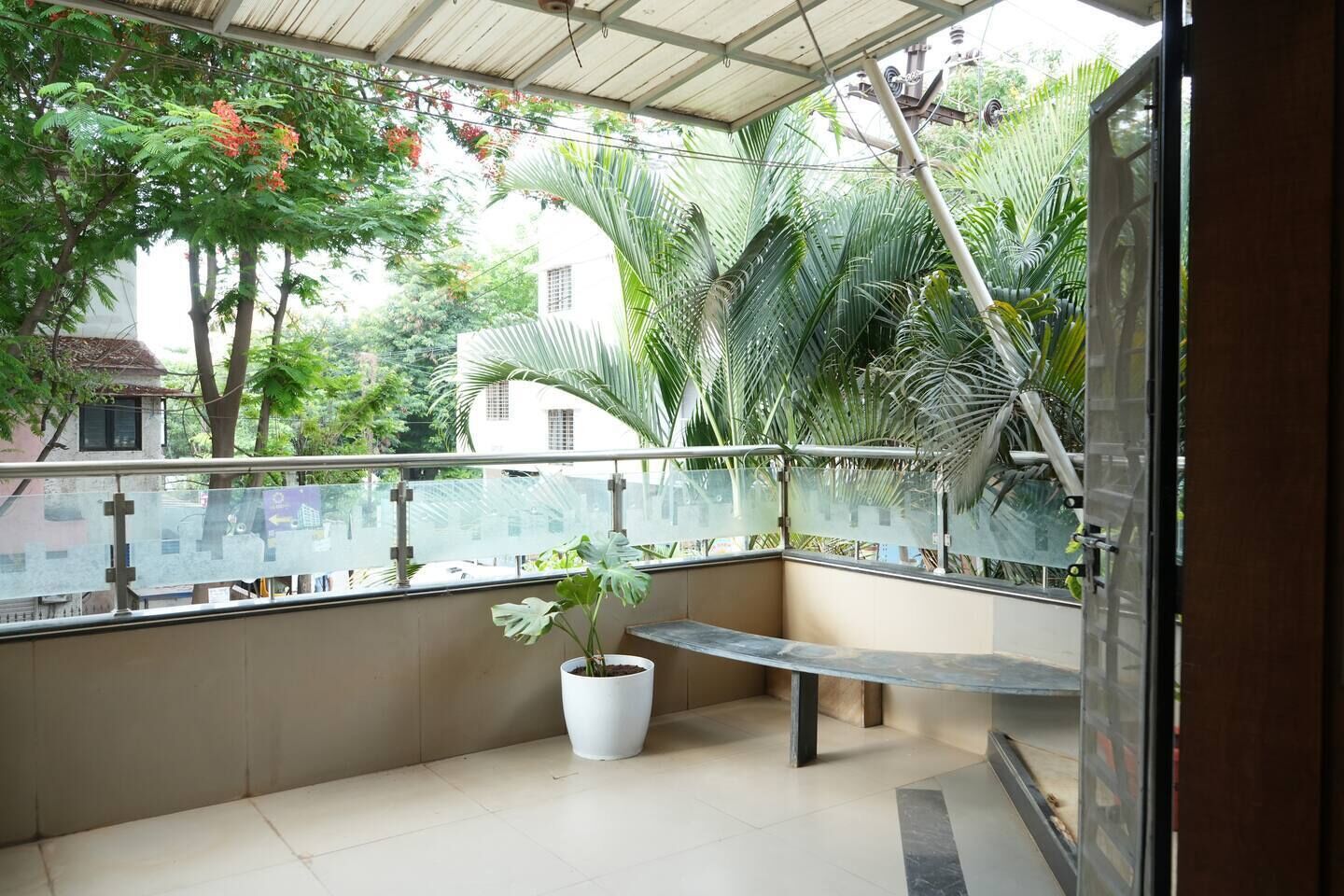 A balcony with a potted plant, a bench, and a view of surrounding greenery and buildings.