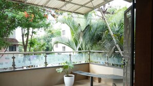 A balcony with a potted plant, a bench, and a view of surrounding greenery and buildings.