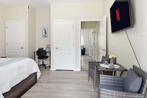 Habitación de hotel con cama, escritorio con silla, zona de comedor con mesa y sillas, y televisión montada en la pared.