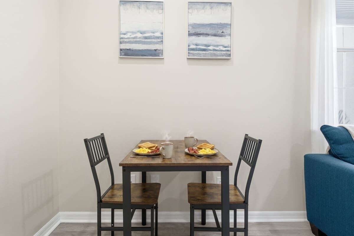Uma sala de jantar com uma mesa de madeira e duas cadeiras, um sofá azul e duas pinturas nas paredes.