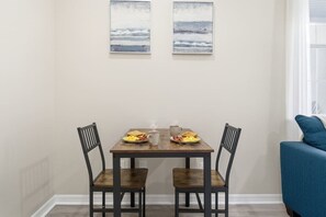 A dining area with a wooden table and two chairs, a blue couch, and two paintings on the wall. - Private Suite near Weeki Wachee Springs (Brooksville)