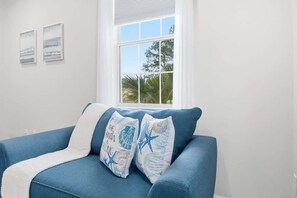 Una habitación con un sofá azul, dos obras de arte colgadas en la pared y una ventana con vistas a palmeras.