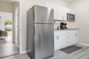 Una cocina moderna con armarios blancos, un refrigerador de acero inoxidable, un microondas y una cafetera.