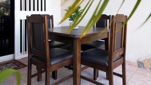 A wooden dining table with four chairs, a potted plant, and a sliding glass door. - Costa Azul Apt: Pool Access Near La Vela Mall (Costa Azul)