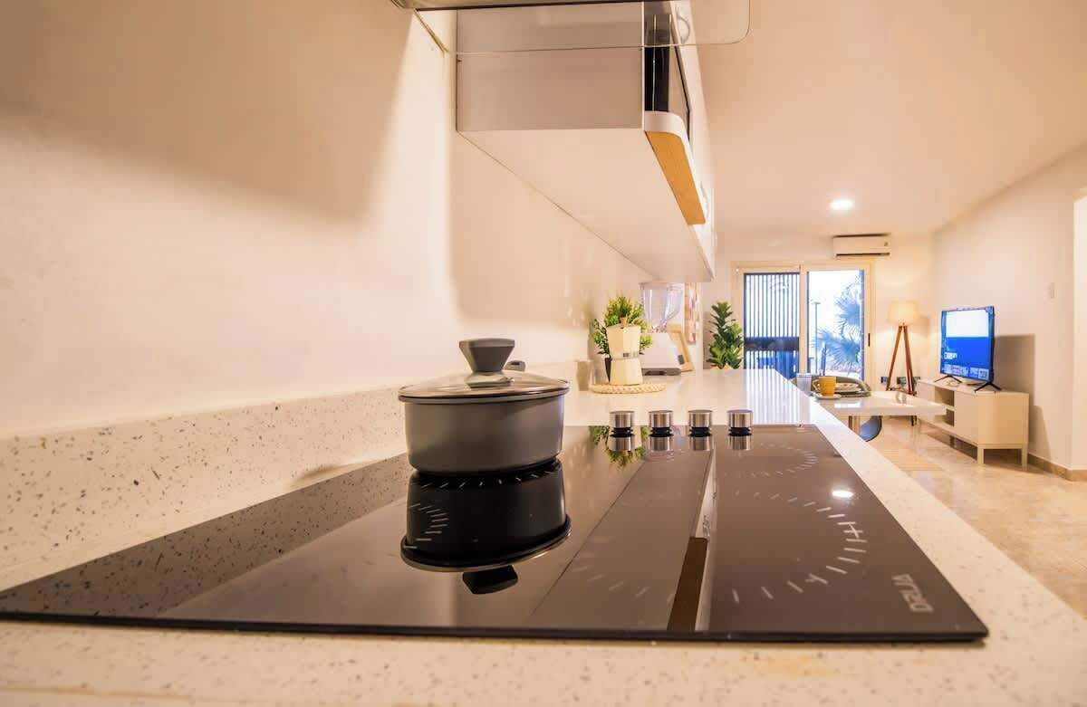 Una cucina moderna con piano cottura a induzione integrato, una pentola sul piano cottura e vista sull'area soggiorno sullo sfondo.