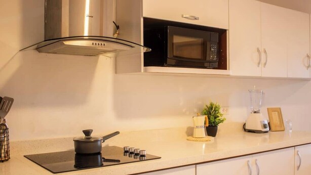 A kitchen with white cabinets, a stainless steel range hood, a microwave, a blender, and a small potted plant. - Costa Azul Apt: Pool Access Near La Vela Mall (Costa Azul)
