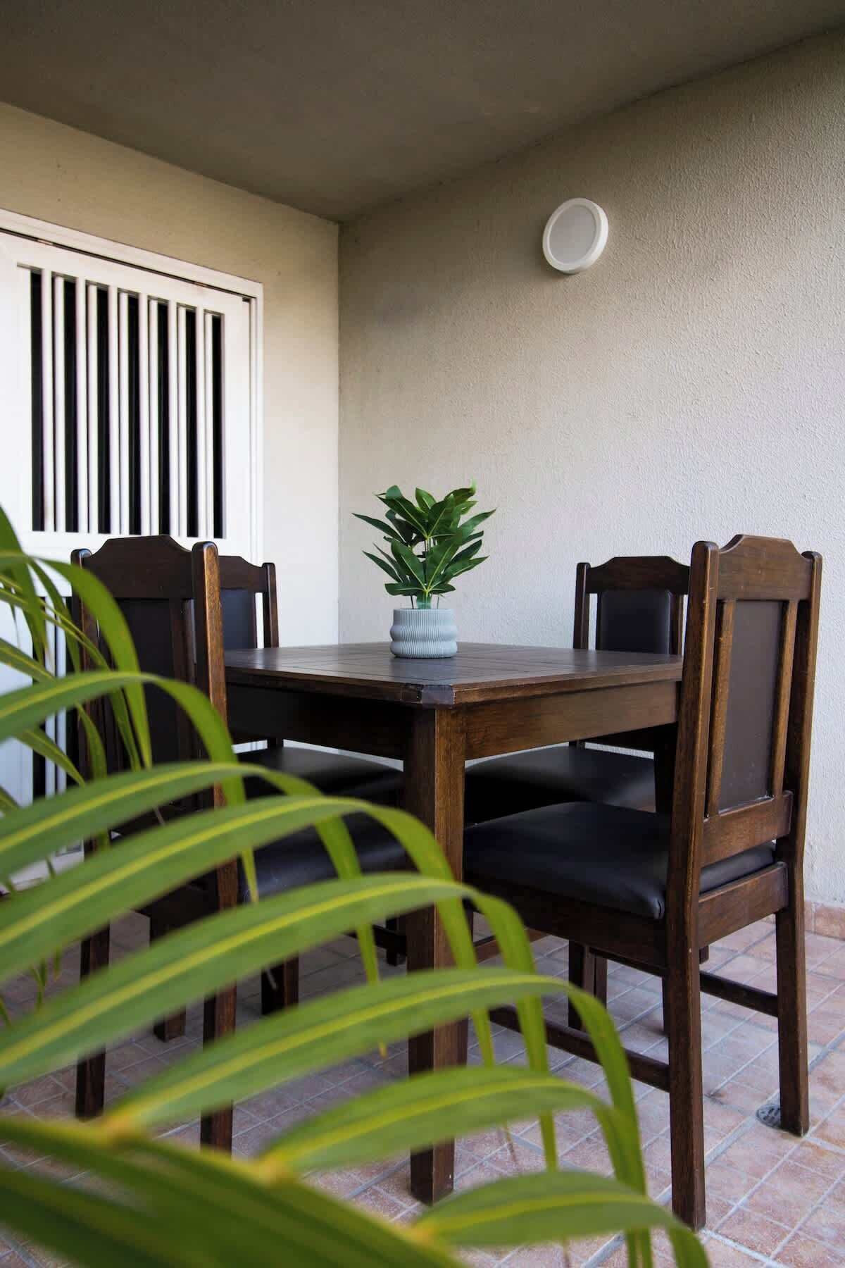 A dining table with chairs, a potted plant, and a window with vertical blinds.