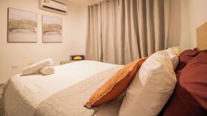 A hotel room with a bed, a pillow, a rolled towel, an air conditioner, and curtains. - Costa Azul Apt: Pool Access Near La Vela Mall (Costa Azul)