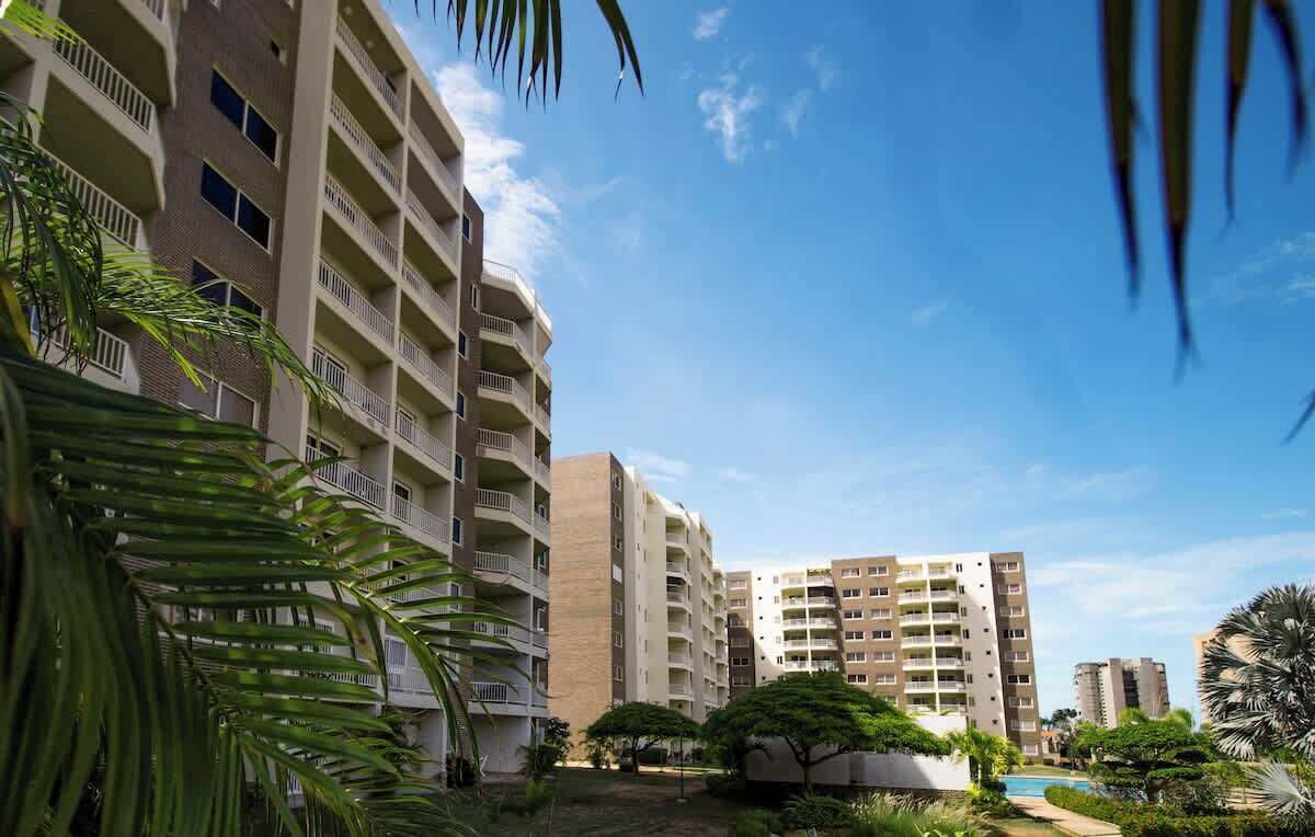 A multi-story residential building with balconies, surrounded by greenery and a clear sky.