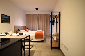 Ein Hotelzimmer mit einem Bett, einem Schreibtisch mit Stuhl, einem Kleiderschrank und einem Fenster mit Vorhängen.
