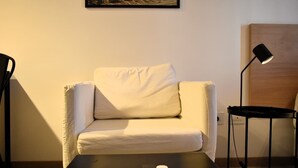 Ein Zimmer mit einem weißen Sofa, einem kleinen Tisch, einer Lampe und einem Gemälde an der Wand.