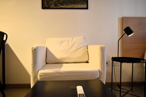 Ein Zimmer mit einem weißen Sofa, einem kleinen Tisch, einer Lampe und einem Gemälde an der Wand.