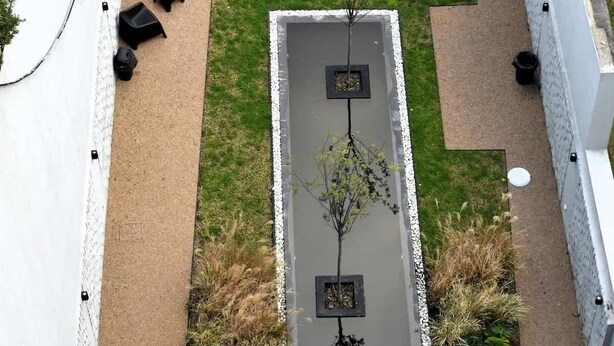 Eine Dachterrasse mit kleinem Rasen, Sitzgelegenheit und einem Pflanzgefäß mit einem Baum.