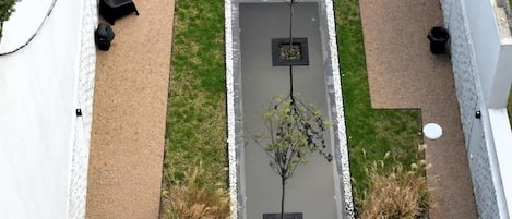 Une terrasse sur le toit avec une petite pelouse, un espace salon et un jardinier avec un arbre.