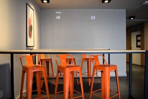 Ein Raum mit einem langen Tisch und vier orangefarbenen Barhocker.
