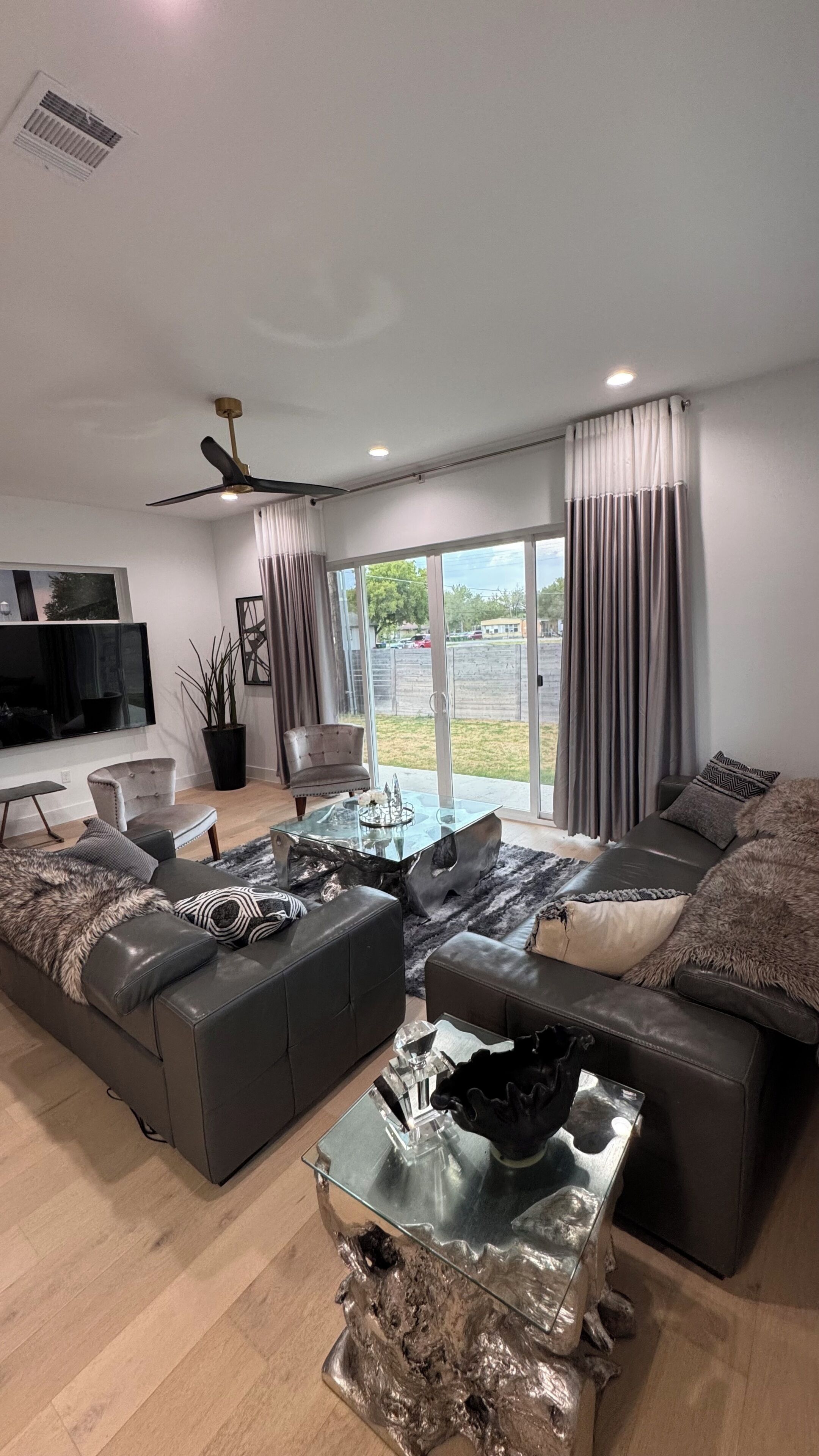 A modern living room with a sectional sofa, a glass coffee table, and a flat-screen TV mounted on the wall.