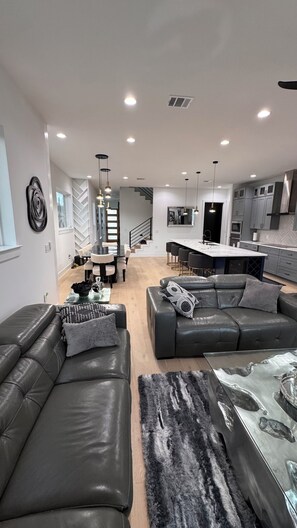Ein modernes Wohnzimmer mit Ledersofas, einem Essbereich und einer Küche mit grauen Schränken.