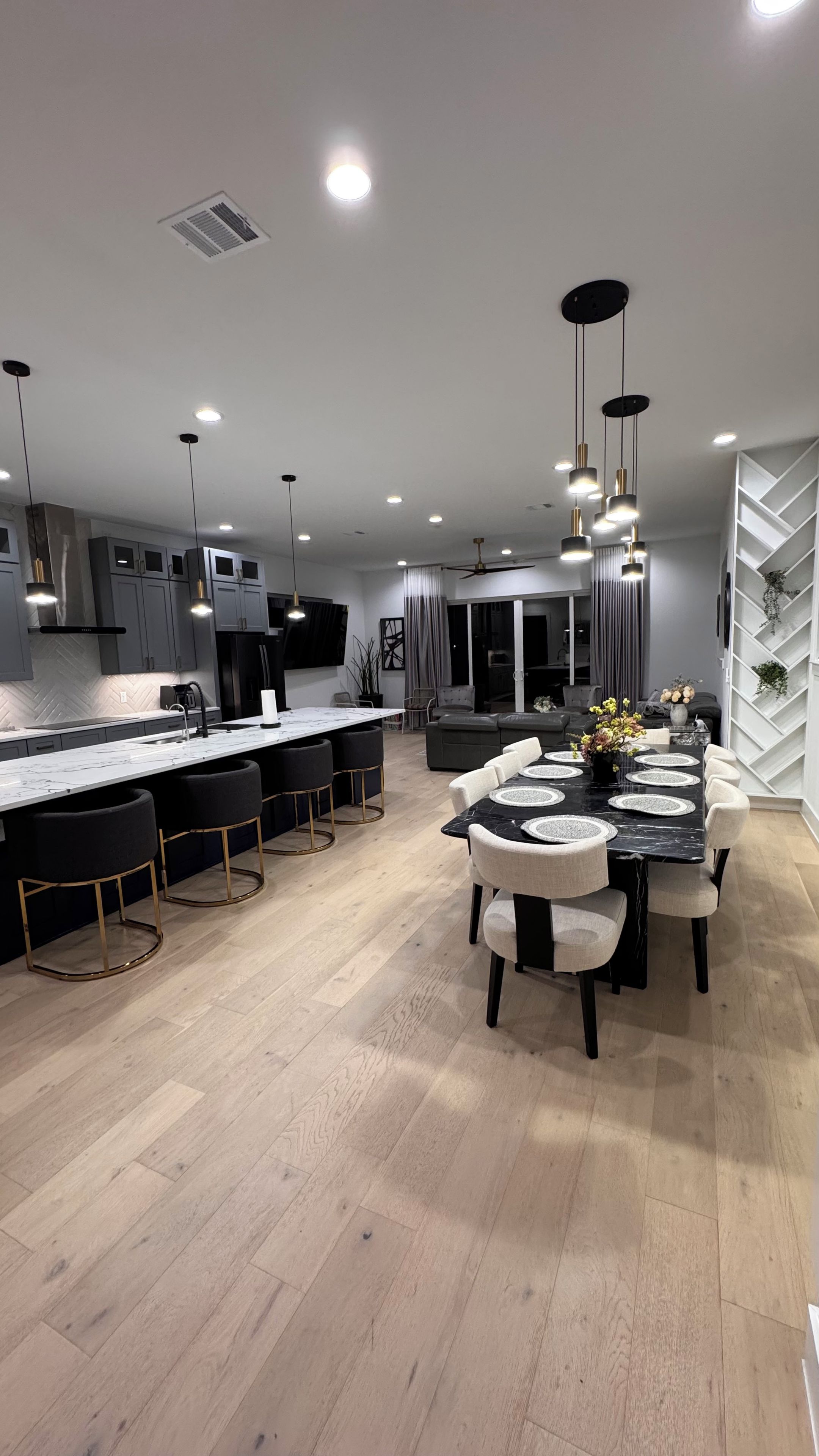 A modern kitchen with a central island, pendant lighting, and a dining area with a marble table and upholstered chairs.