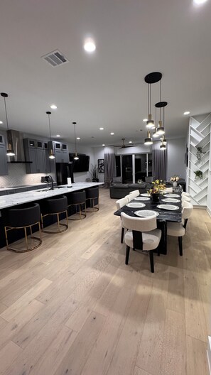 Une cuisine moderne dotée d’un îlot central, de luminaires suspendus et d’un coin repas avec une table en marbre et des chaises rembourrées.