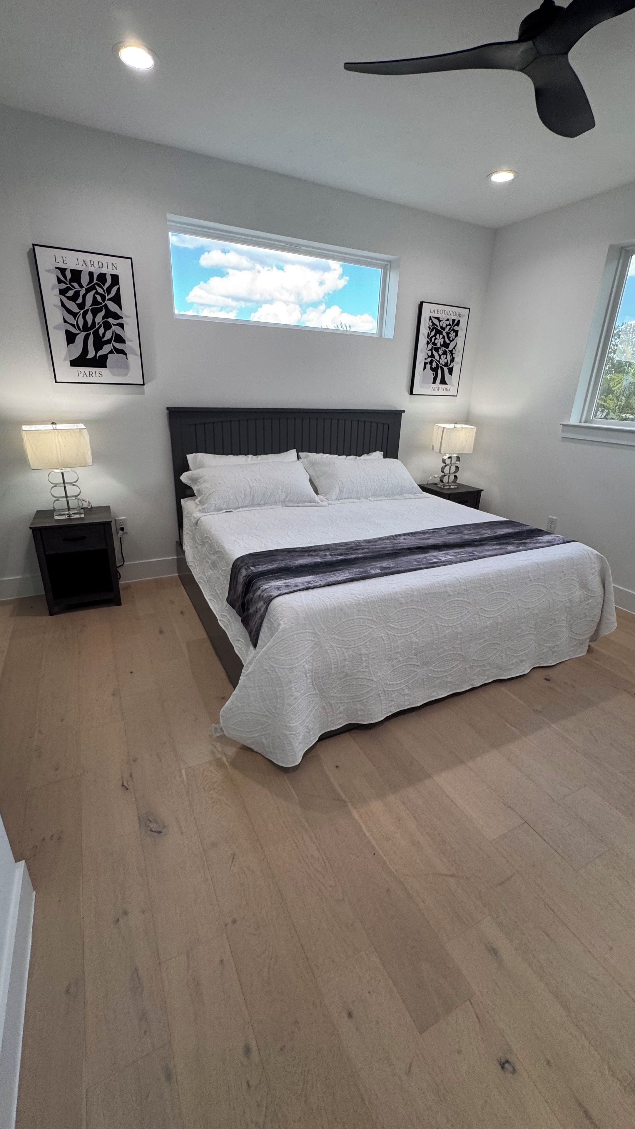 A bedroom with a bed, two nightstands, a ceiling fan, and artwork on the walls.