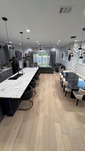 Eine moderne Küche mit Marmorarbeitsplatte, ein Essbereich mit einem schwarzen Marmortisch und eine Sitzecke mit Sofas und Sesseln.