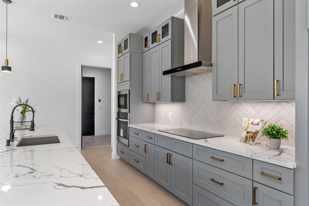 Une cuisine moderne avec des meubles gris, un plan de travail en marbre blanc et un dosseret de carreaux disposés en motif chevron.
