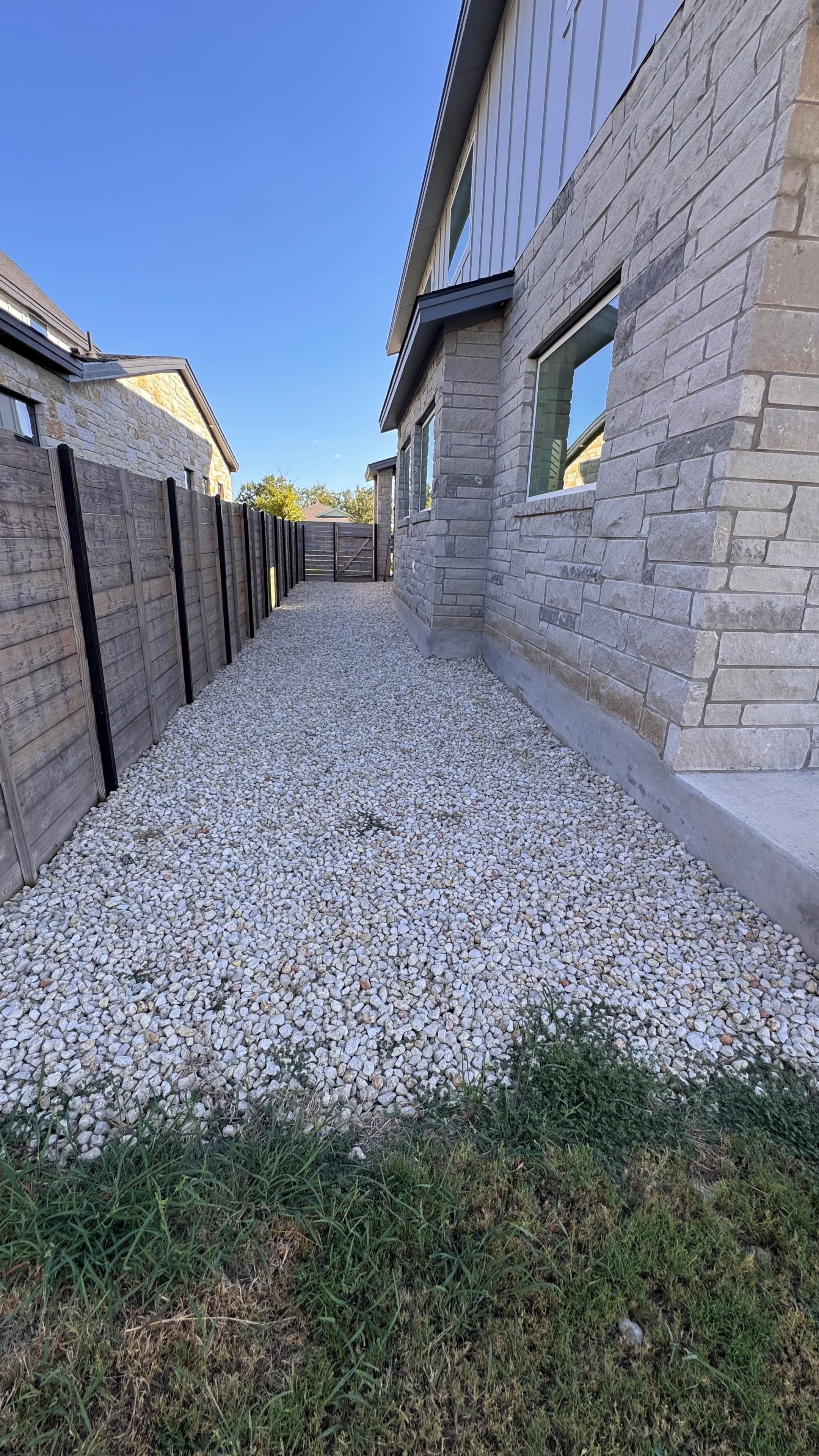 A gravel driveway leading to a house with stone walls and a wooden fence.