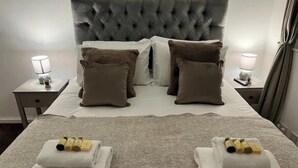 Ein ordentlich bezogenes Bett mit einem gepolsterten Kopfteil, zwei Kissen und zwei Nachttische mit Lampen.