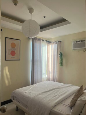A bedroom with a bed, a ceiling light fixture, a wall-mounted air conditioning unit, and a framed picture. - JFS Cozy 1-bedroom Staycation in beautiful Manila - Near US Embassy (Manila)