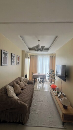 A living room with a sofa, a dining table, and a TV mounted on the wall. - JFS Cozy 1-bedroom Staycation in beautiful Manila - Near US Embassy (Manila)